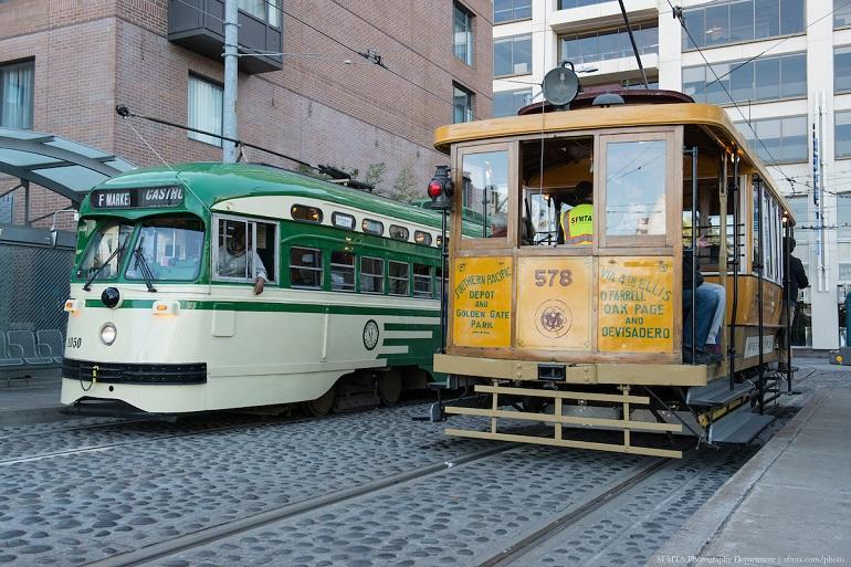 Vintage green and cream streetcar passing a historic yellow cable car on city street.