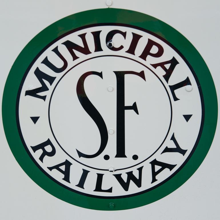SF Municipal Railway circular seal with green border, white center, and black text reading "MUNICIPAL RAILWAY" around "S.F." initials.