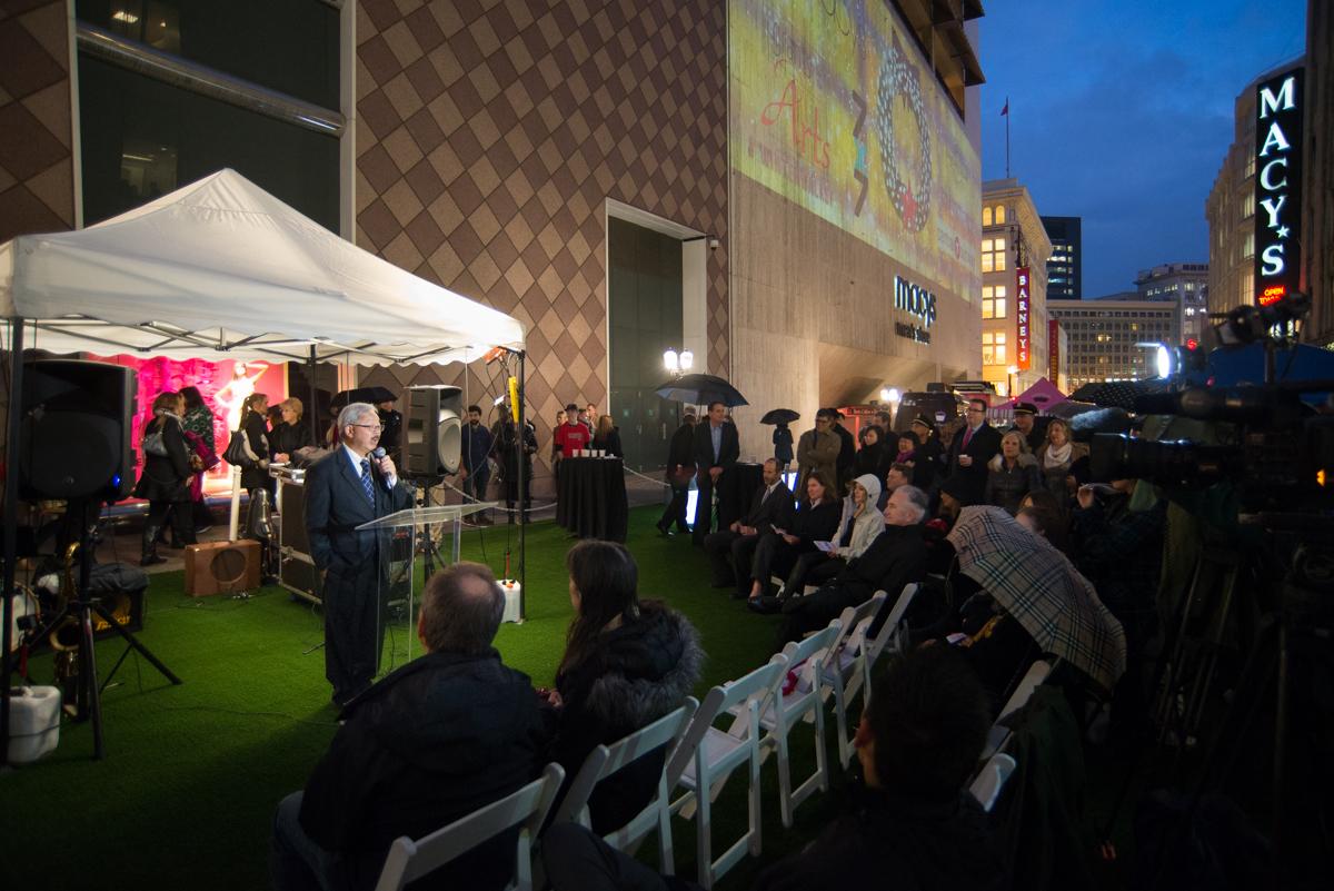 Mayor addresses crowd at outdoor Winter Walk event in front of Macy's building at dusk.