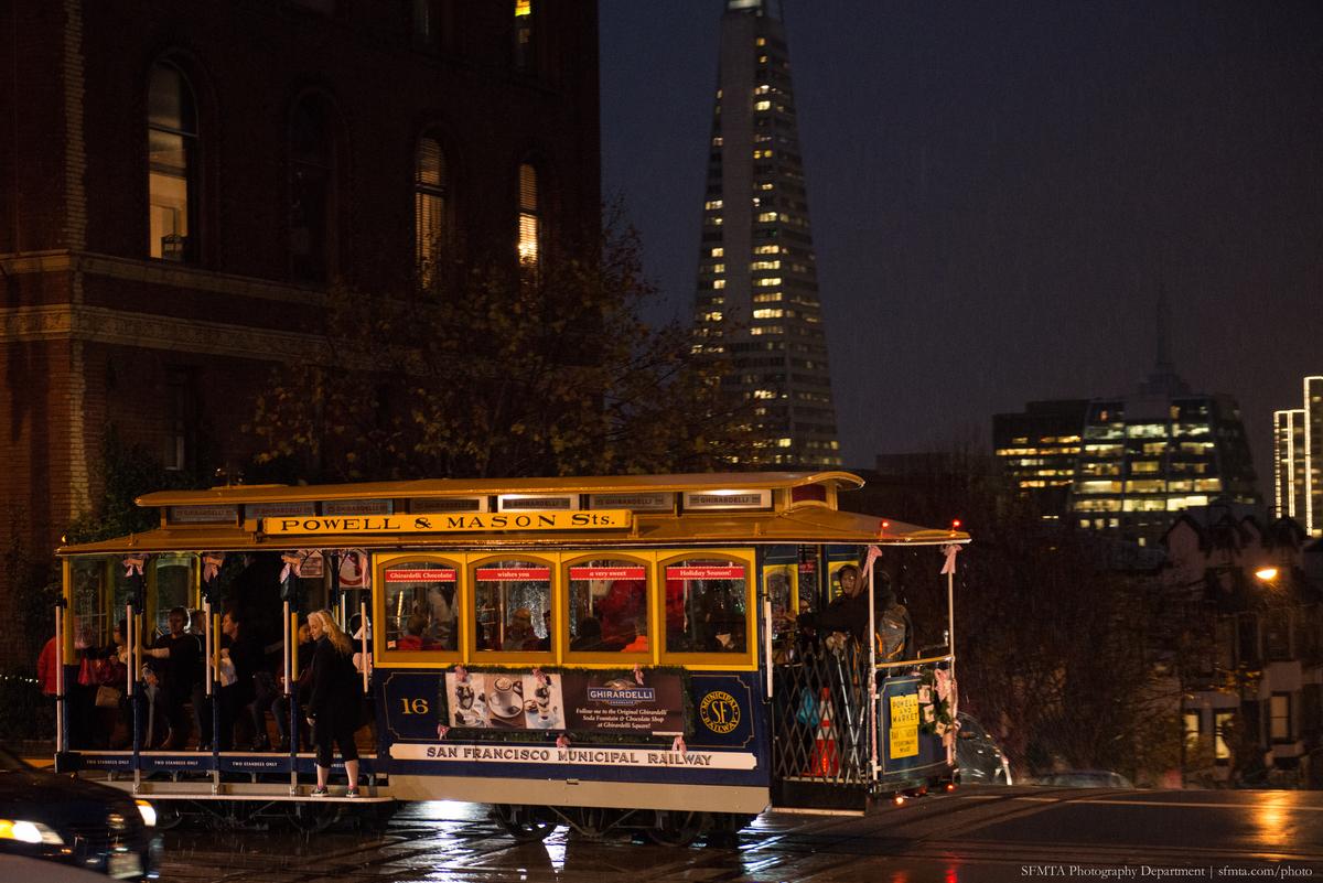 Powell & Mason cable car at night on California Street with San Francisco skyline in background.