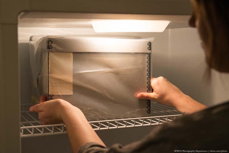 Person placing wrapped archival box into cold storage freezer for photograph preservation.