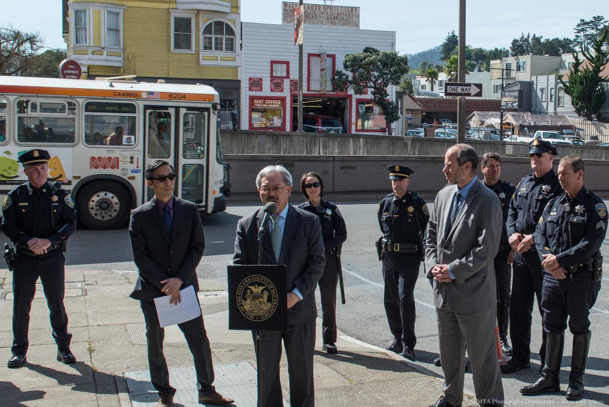 Mayor Lee speaks at press conference with officials and police officers on Geary Street corner with 38 Geary bus in background.