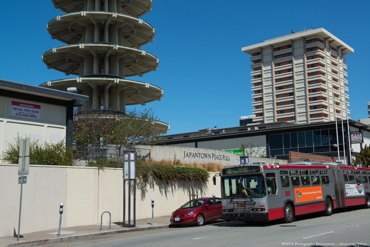 Red and orange bus stopped at Japantown Peace Plaza with pagoda and residential tower visible behind.