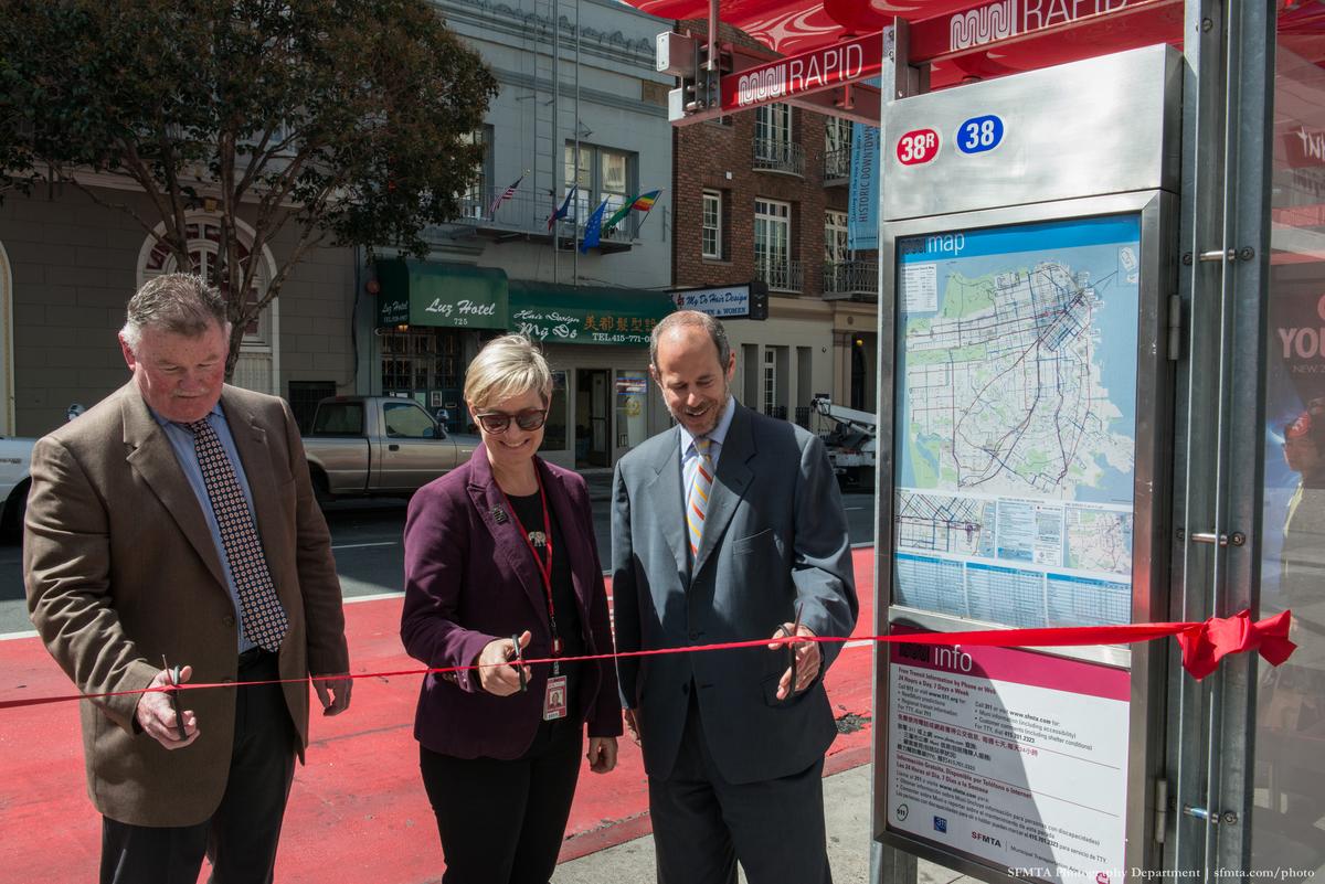 Three officials cut red ribbon at Muni Rapid transit shelter on Geary Street during dedication ceremony.