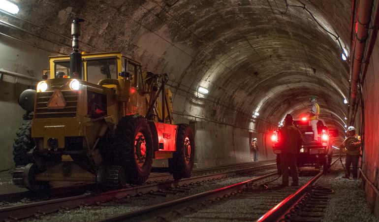Heavy equipment and workers inside illuminated tunnel during trackway construction.