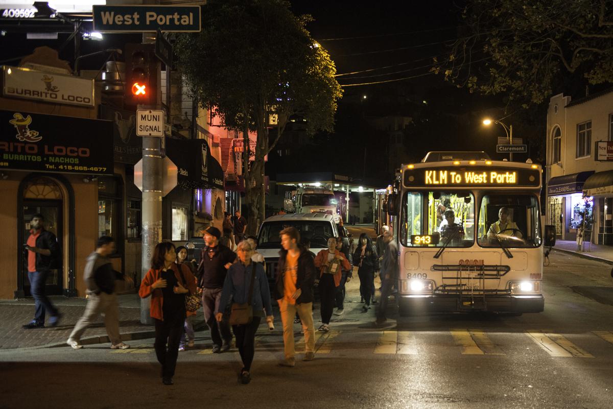 Bus shuttle at West Portal Station with passengers boarding at night on city street.