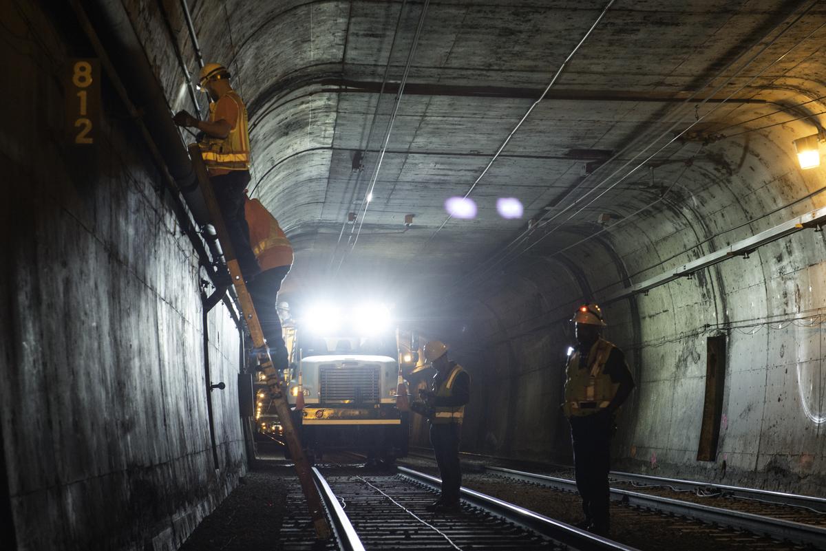 Workers install cable brackets on tunnel wall during subway construction beneath Twin Peaks.