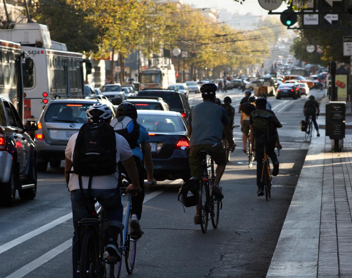 Cyclists riding on a city street with cars and a bus during daytime commute.