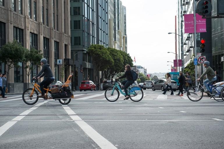 People riding bikes through an urban intersection on Market Street at 10th Street.