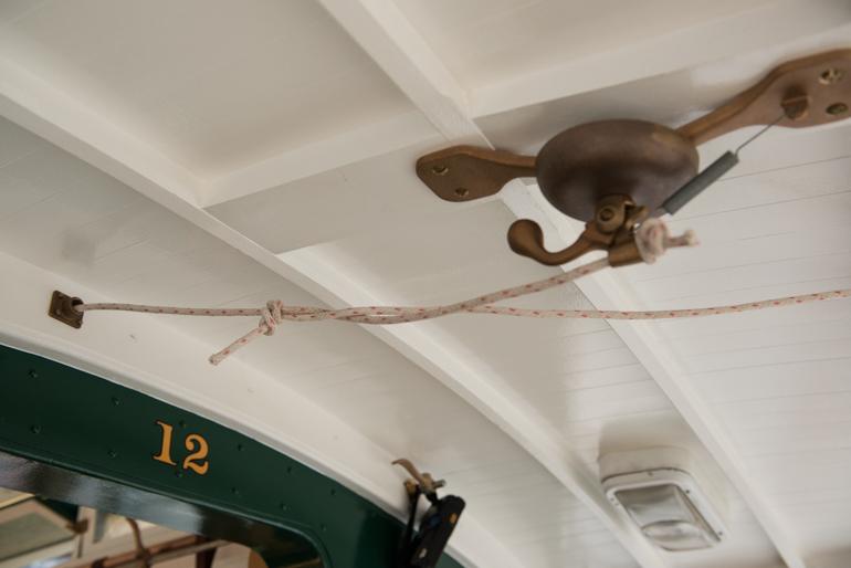 Conductor's bell mounted on ceiling of Cable Car 12 with rope pull and green car number 12 visible below.