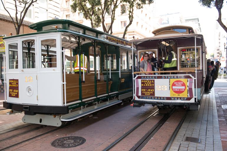 Two cable cars passing on Powell Street near Market, one empty and one with passengers aboard.
