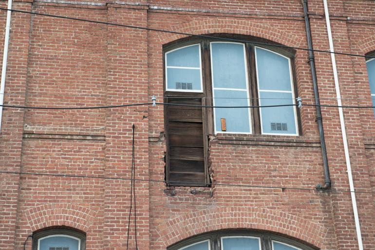 Red brick building facade with dark wooden door and three large windows with white frames and horizontal muntins.