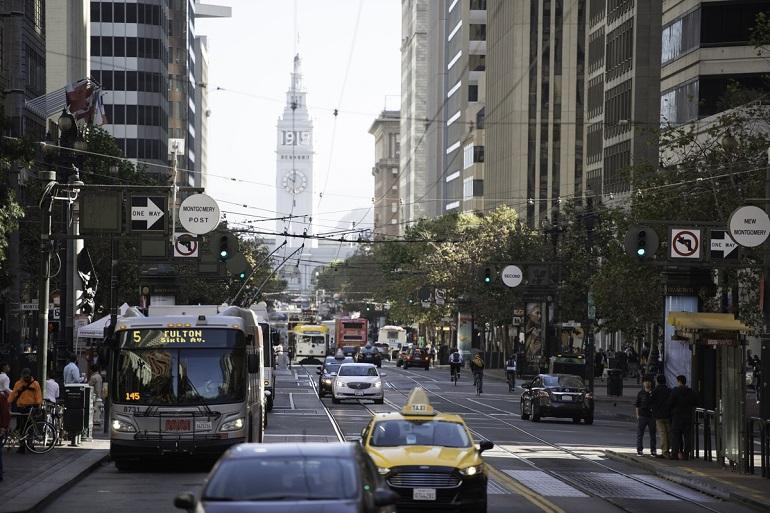 Market Street downtown with Muni bus, taxis, pedestrians, and Ferry Building visible in background.