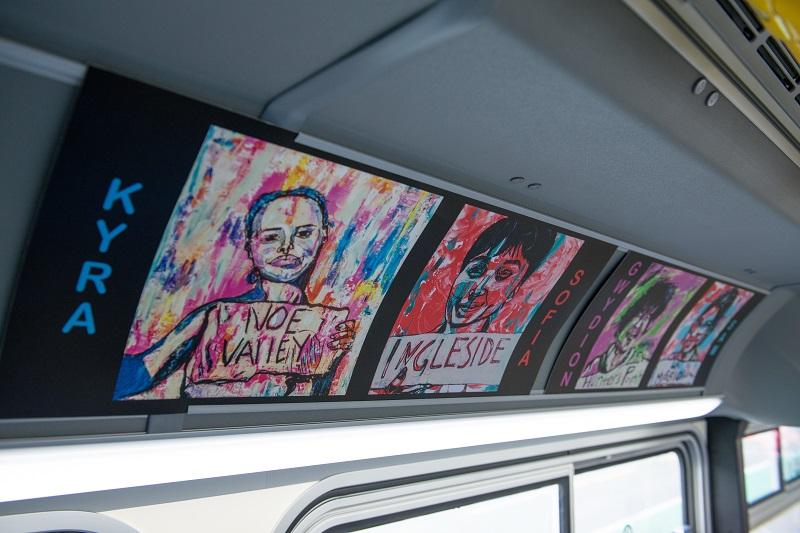 Colorful pop art portraits displayed on interior transit vehicle signage, featuring stylized faces with text overlay in vibrant colors.