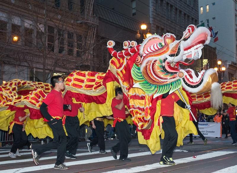 Performers carry a large red and gold dragon with green accents through a city street during a parade.