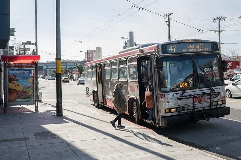 Bus 47 stops at a transit bulb on a city street with passengers boarding.