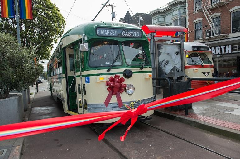 Historic green and cream streetcar decorated with red bow at ribbon-cutting ceremony on Market Street.