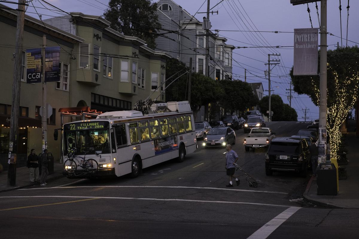 22 Fillmore trolley bus traveling east on 18th Street at dusk with holiday-lit trees lining the street.