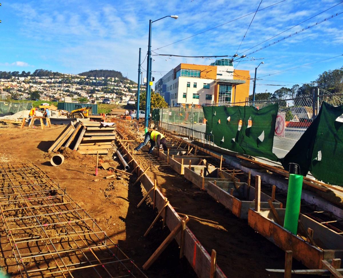 Construction site with excavation, reinforced concrete foundation, and yellow building under development on hillside.