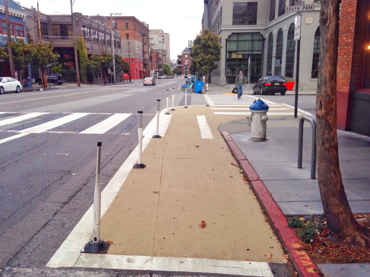 Painted safety zone with bollards separating pedestrians from vehicle traffic on urban street corner.