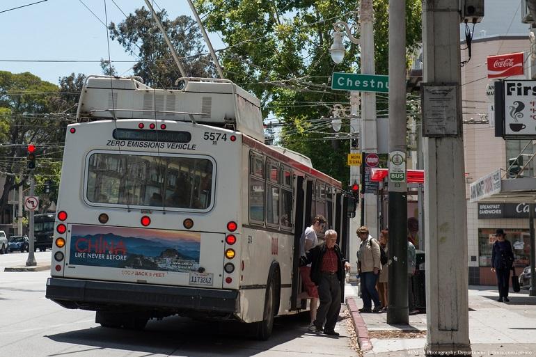 30 Stockton trolley bus stopped at curb with passengers boarding at shelter stop on city street.