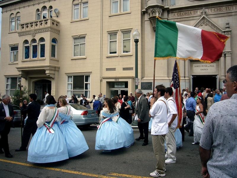 Italian Festival parade procession on city street with participants in blue dresses and Italian flag.