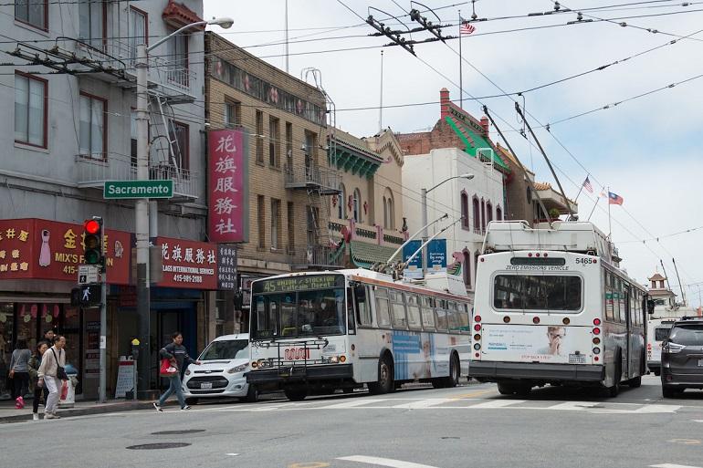 Two Muni buses on Sacramento Street in San Francisco's Chinatown neighborhood with historic buildings and storefronts.