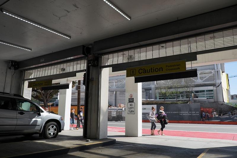A car exits an underground parking garage while pedestrians walk on the red sidewalk outside.