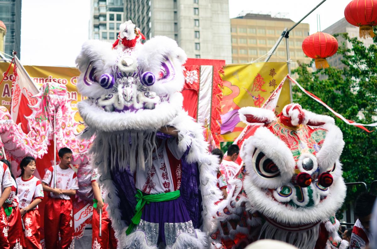 Lion dancers in white and purple costumes perform at Chinatown Autumn Moon Festival with red lanterns and decorative banners.