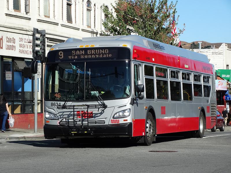 Red and white bus number 9 stopped at traffic light on city street