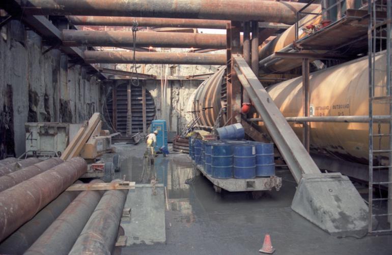 Workers and equipment at Muni Metro Turnback construction site with tunnel entrances and excavation area.