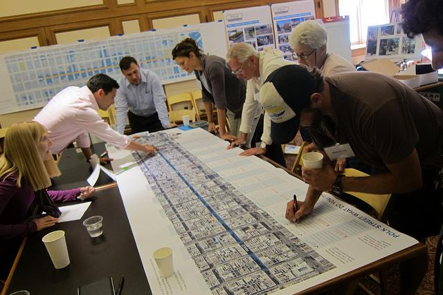 Group of people reviewing a large transit or street planning map at a community outreach meeting.
