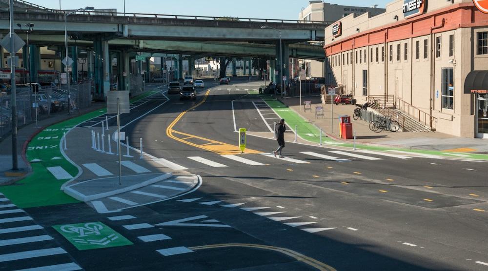Newly upgraded intersection at 9th and Division streets with green bike lanes, white crosswalks, and elevated transit station overhead.