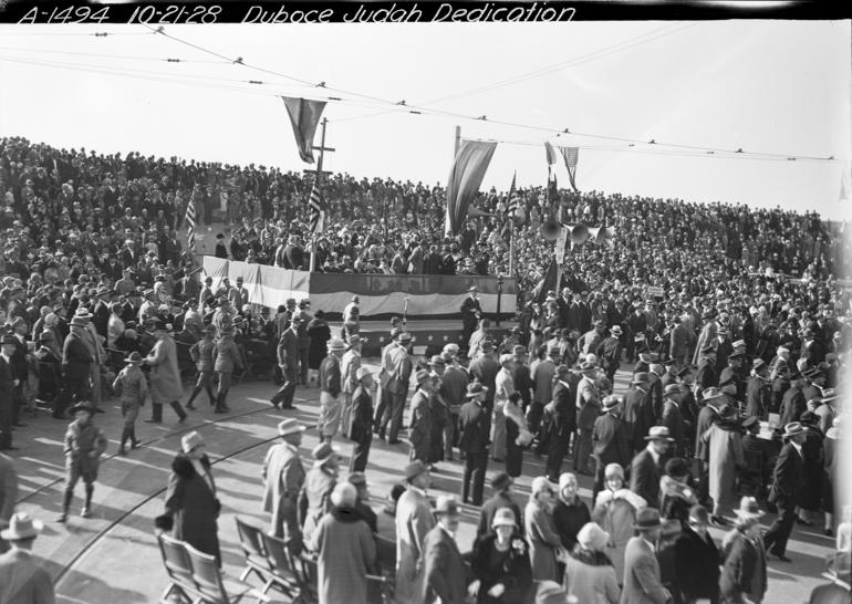 Large crowd gathered around central pavilion with flags and banners at N Judah Line dedication ceremony, 1928.