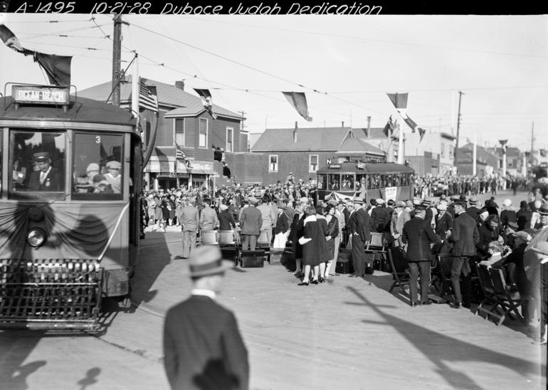 Large crowd gathered on street with streetcars and American flags for N Judah Line dedication, 1928.