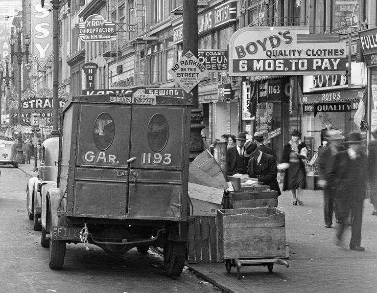 Vintage truck parked on busy Market Street near 8th Street with pedestrians and storefronts visible, 1930s.