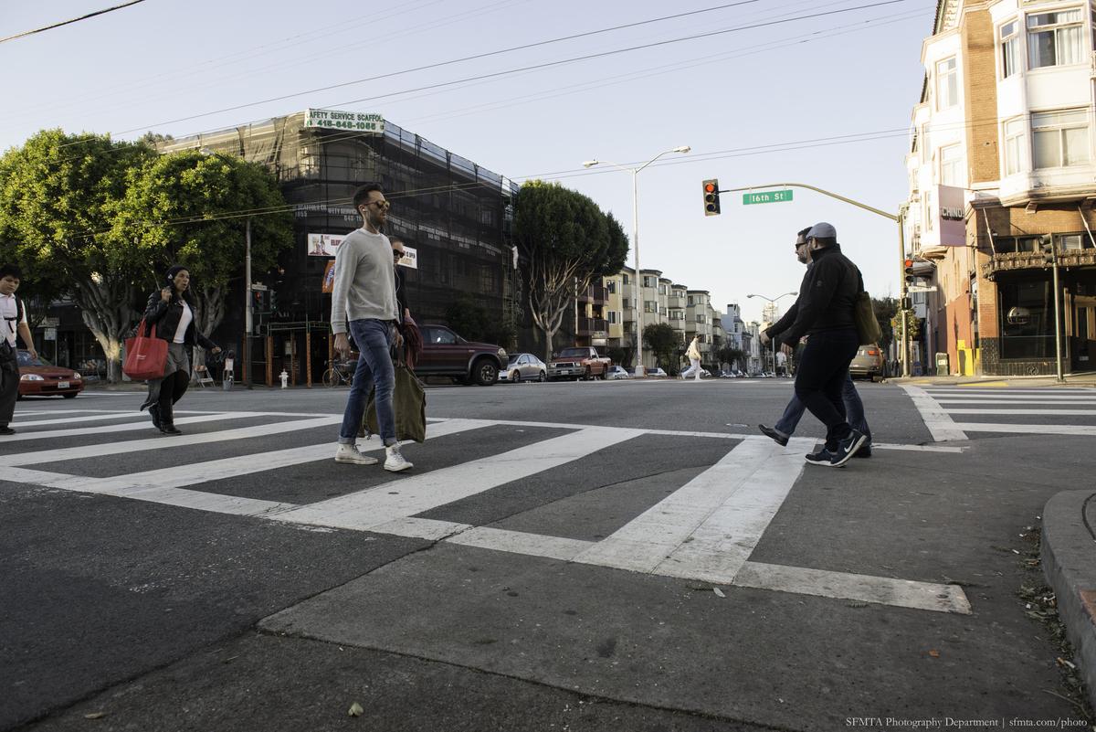 Pedestrians crossing a zebra-striped crosswalk at 16th and Guerrero streets in San Francisco.