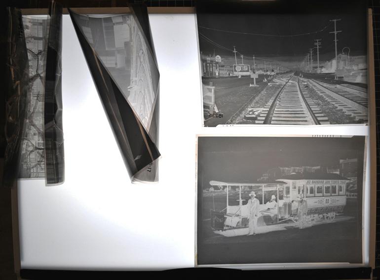 Deteriorated and well-preserved cellulose acetate film negatives displayed on lightbox, showing railroad and transit vehicle photographs.