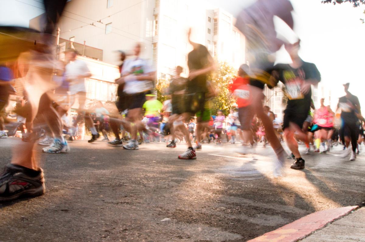 Blurred motion of runners participating in Bay To Breakers race on city street with buildings and spectators.
