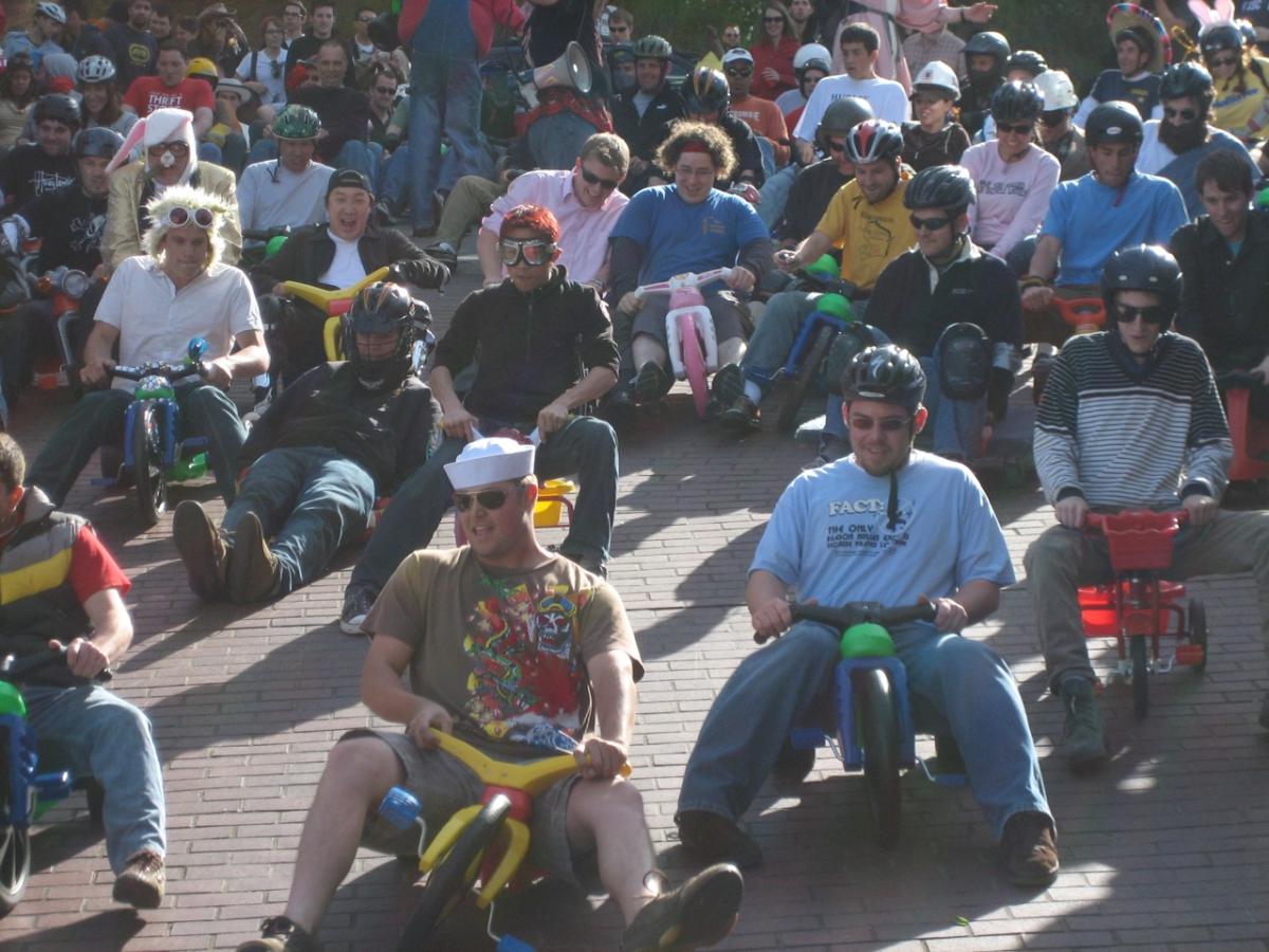 Large crowd of people riding big wheels down a brick street during daytime event.
