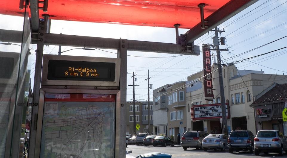 Muni bus shelter with red canopy, digital NextMuni sign displaying route 31-Balboa arrival times, and transit map.