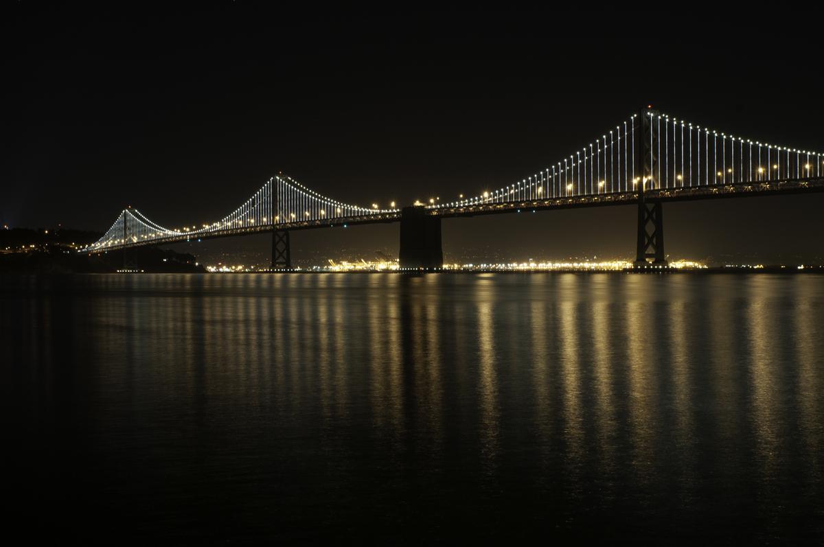 Bay Bridge western span illuminated at night with reflections on water below