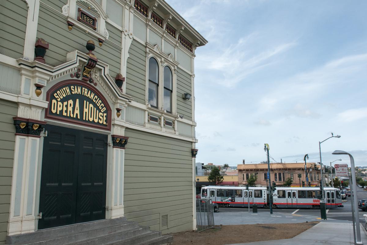 South San Francisco Opera House facade with Muni T Third light rail vehicle passing by.
