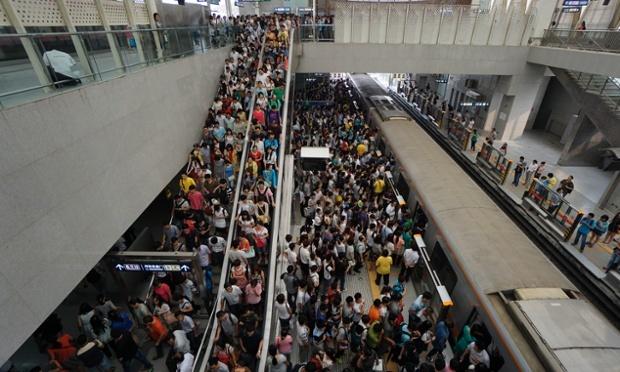Crowded subway platform with passengers waiting on multiple levels during peak hours.