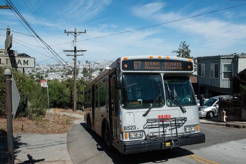 # Alt Text</p>
<p>Muni bus 8523 on Route 67 traveling through Bernal Heights with San Francisco skyline in background.