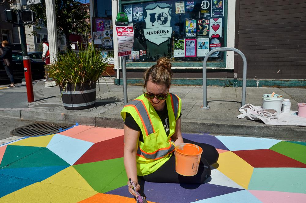 Worker in safety vest painting colorful geometric mural on street for bike corral installation.