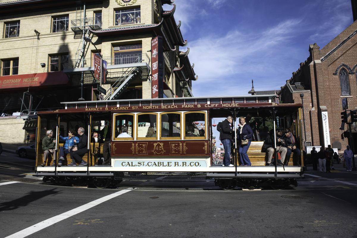California Cable Car traveling on California Street with passengers boarding and historic San Francisco buildings in background.