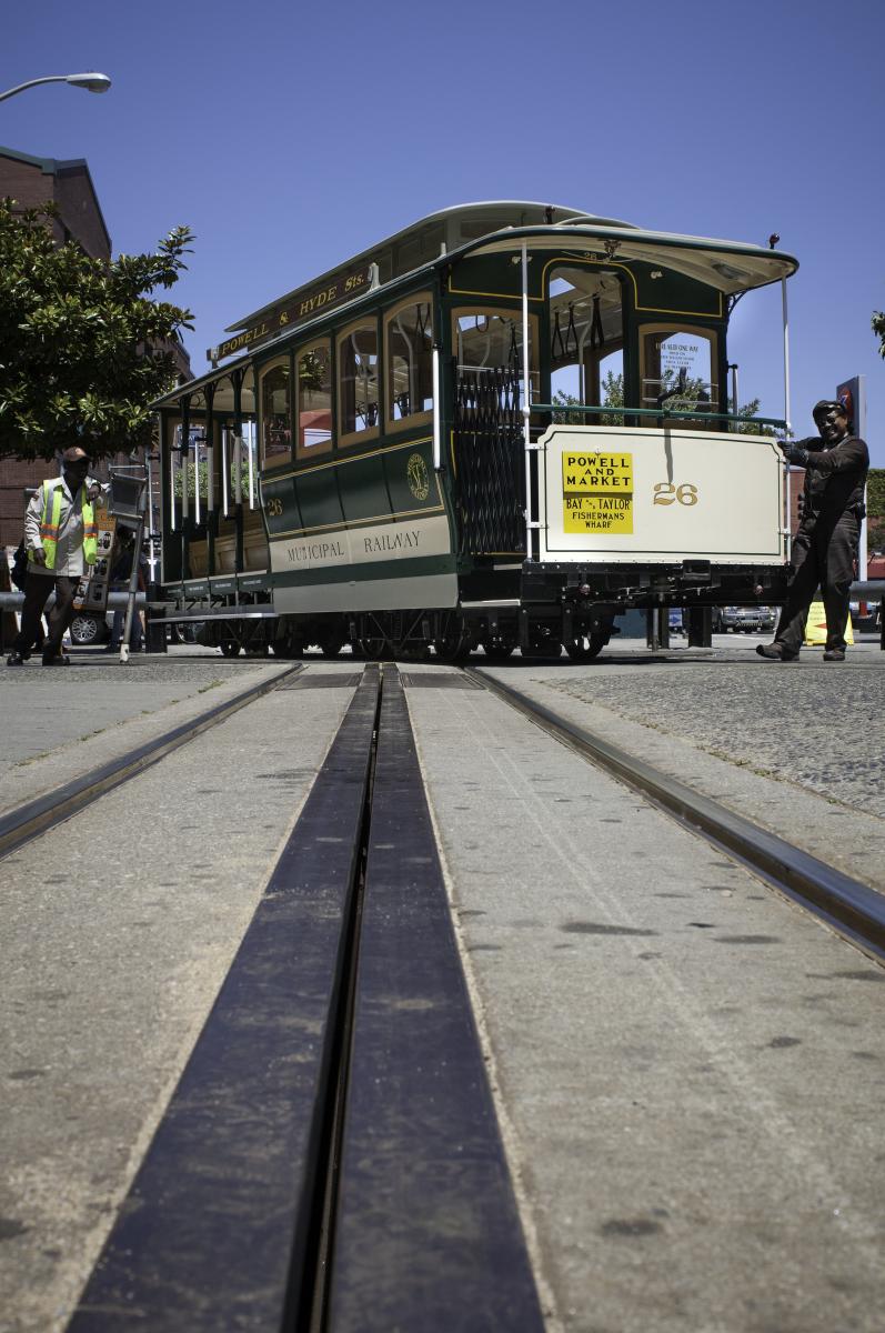Cable car 26 stopped on tracks at turntable with conductor and gripman in uniforms, viewed from track level.