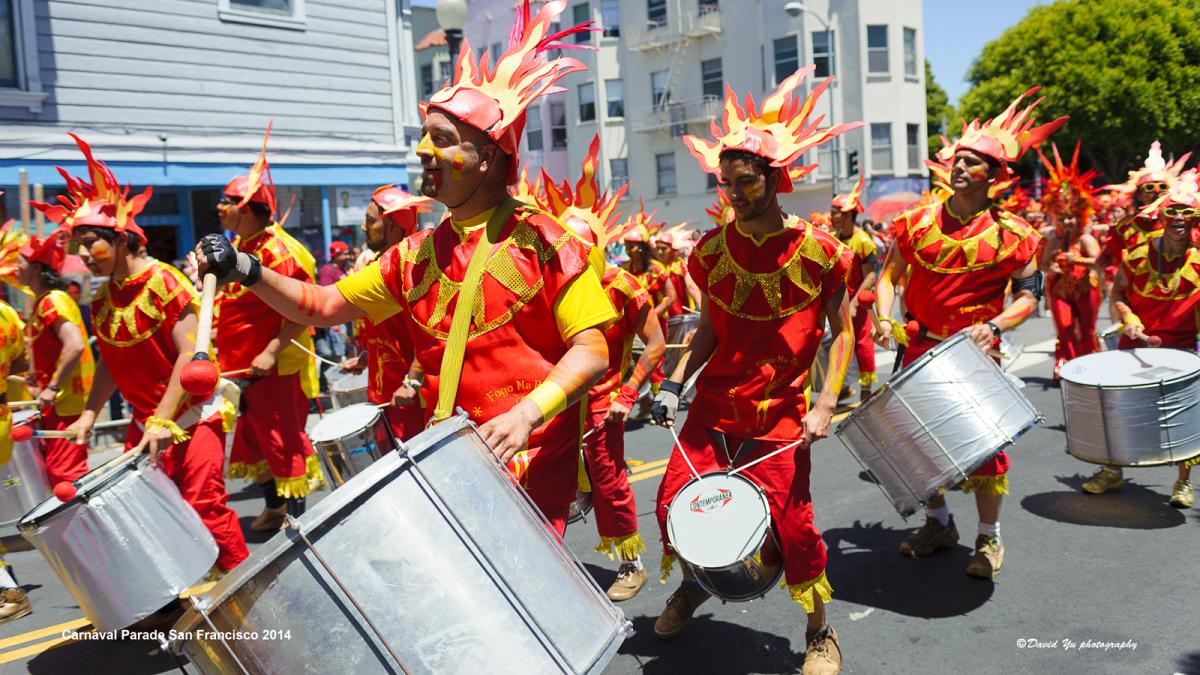 Drummers in red and yellow costumes with feathered headdresses perform during the San Francisco Carnaval Parade.