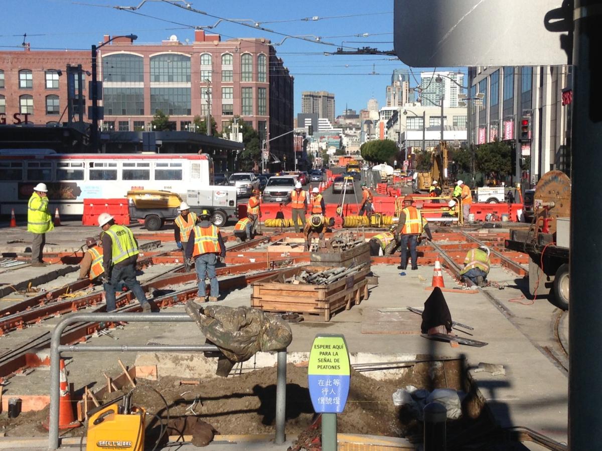 Construction crew working on transit track at 4th and King Street with equipment and vehicles.